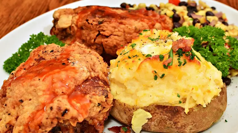 Loaded baked potato with cheesy topping alongside fried chicken on a restaurant plate – LongHorn Baked Potato