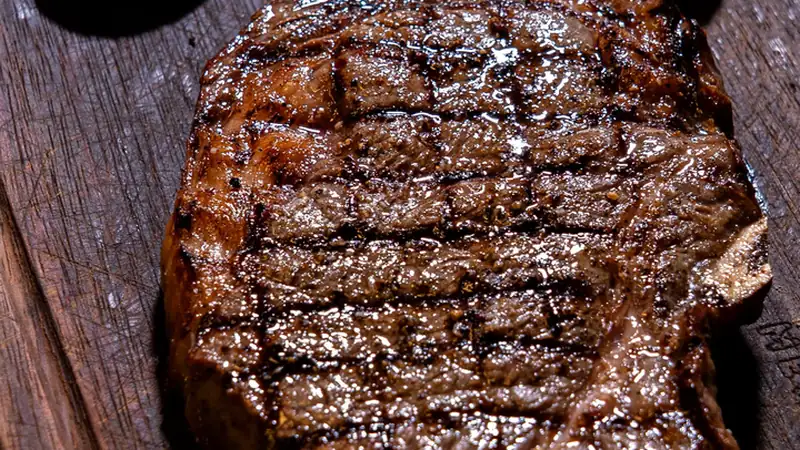 Close-up of a thick fire-grilled boneless ribeye steak with grill marks on a wooden cutting board – LongHorn Outlaw Ribeye
