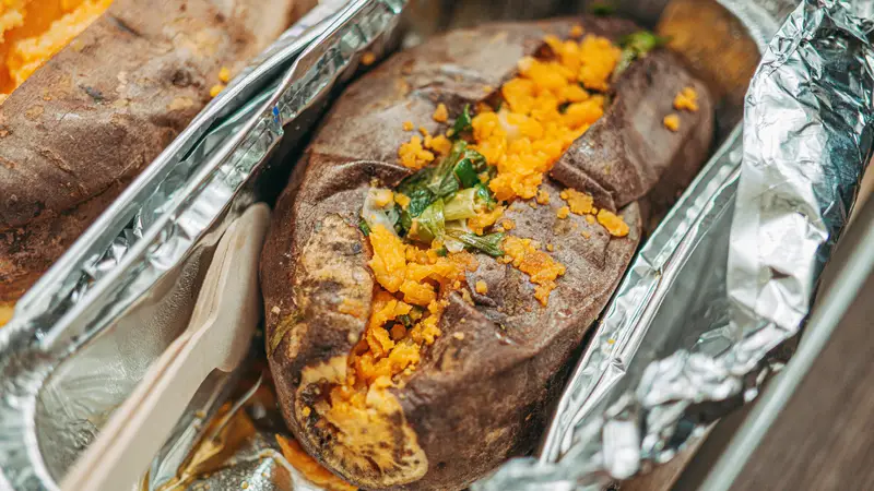 Baked sweet potato split open with bright orange flesh in a foil tray – LongHorn Sweet Potato side